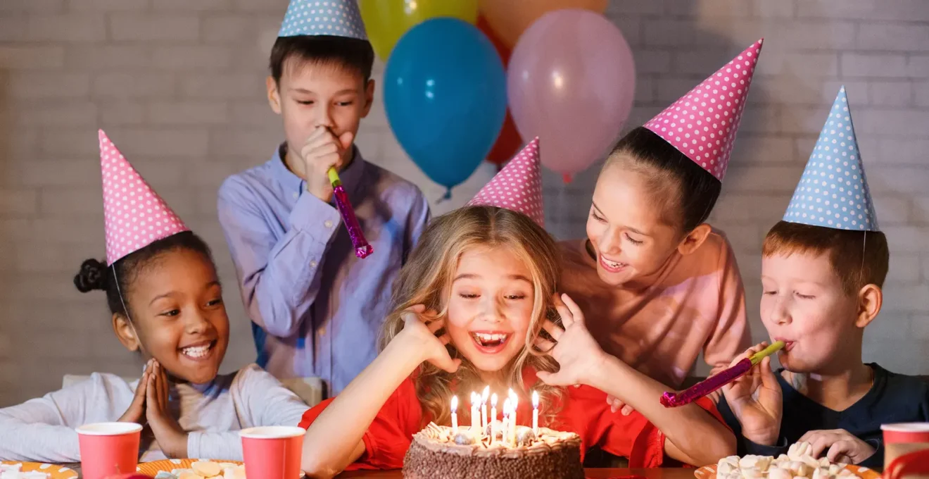 Des enfants fêtent un anniversaire autour d'une table dans le salon d'un parc de trampolines.